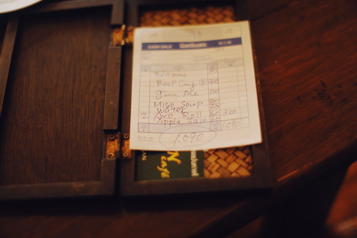 Close-up of a restaurant bill placed on a dark wooden table, creating a moody ambiance.