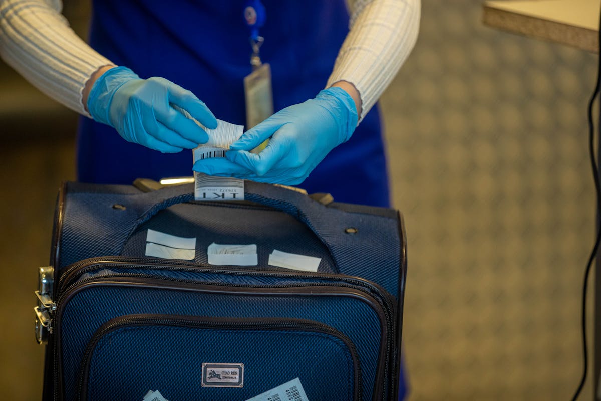 Flying With Cannabis Could Backfire on Americans Despite TSA Guidance 5 Close-up of airport security process with gloved hands inspecting luggage tags.