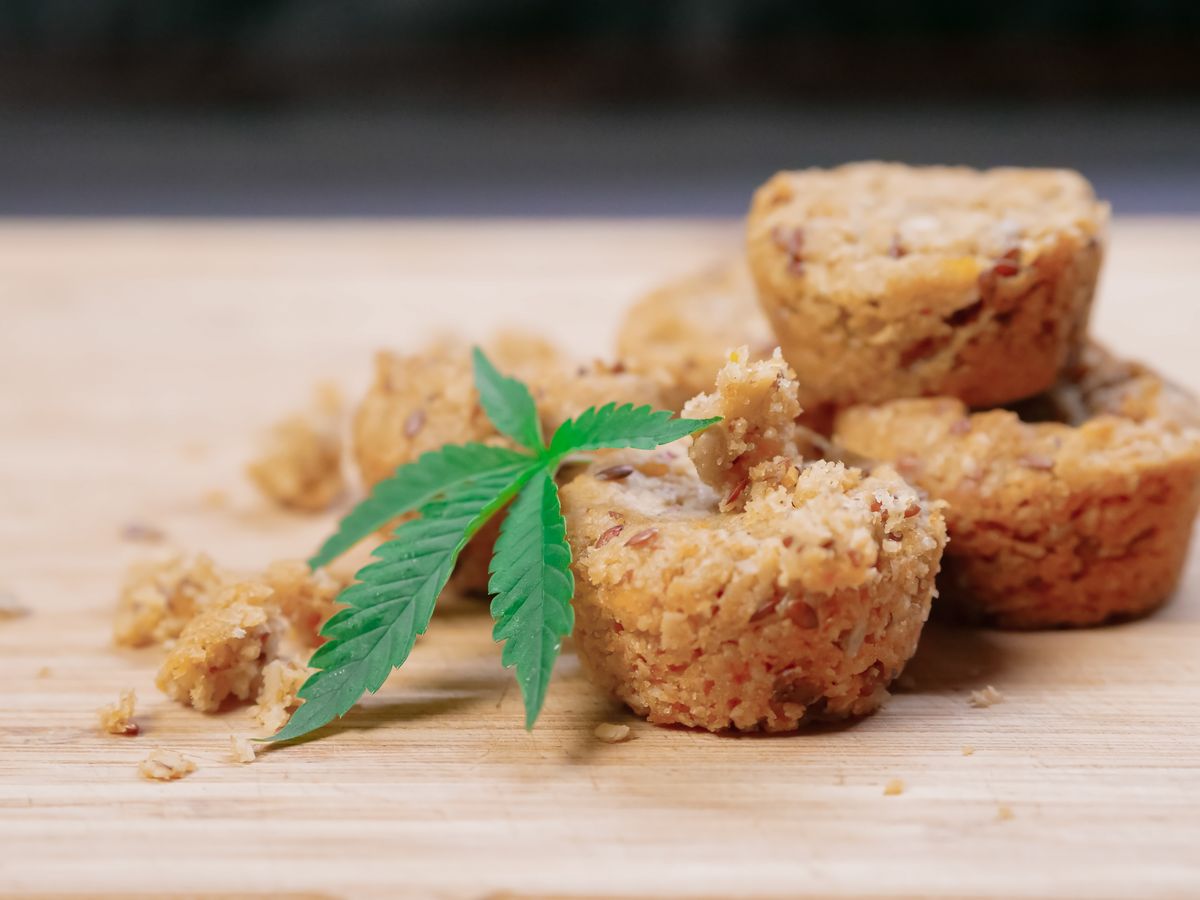 Close-up of cannabis-infused muffins with hemp leaf on a wooden surface.