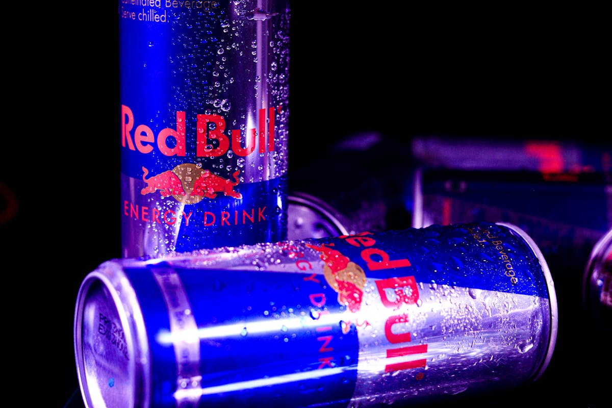 Close-up of chilled Red Bull cans with water droplets, reflecting vibrant neon lighting.