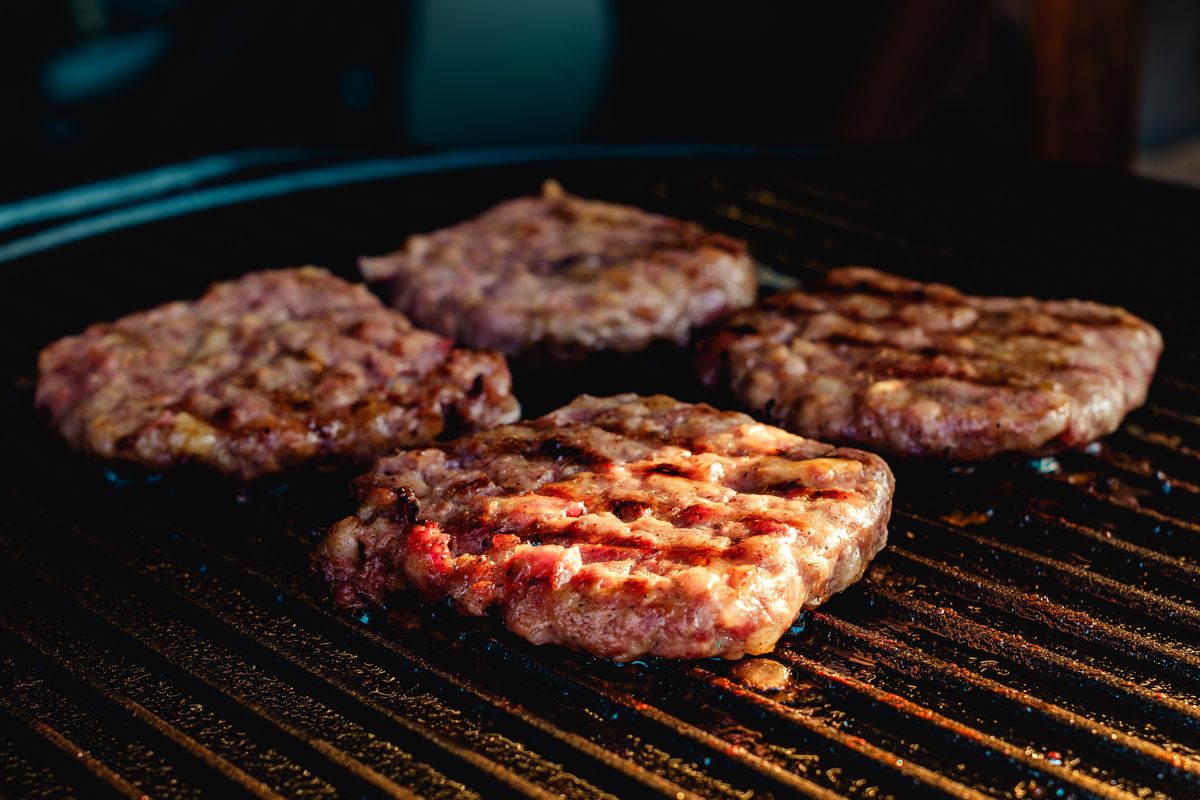 Two Major Suppliers Behind The 714 Pounds Of Beef Served Yearly By McDonald's. 1 Close-up of four juicy burger patties cooking on an outdoor barbecue grill, perfect for summer grilling.