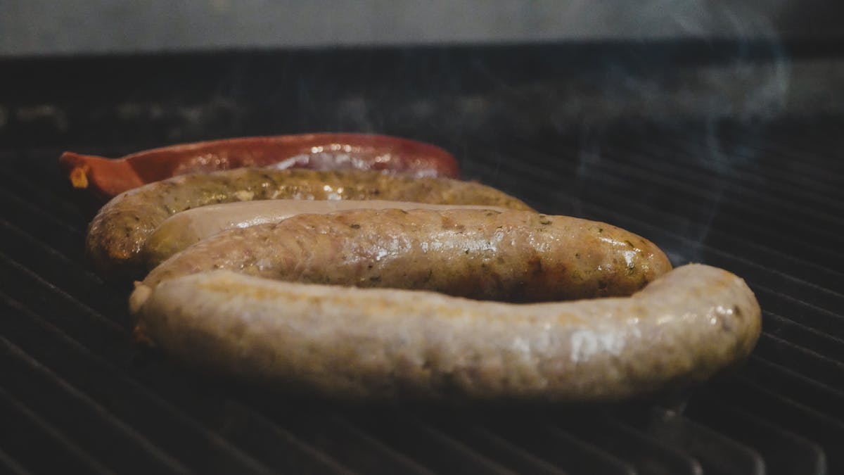 Close-up of juicy sausages smoking on a grill, perfect for summer BBQ themes.