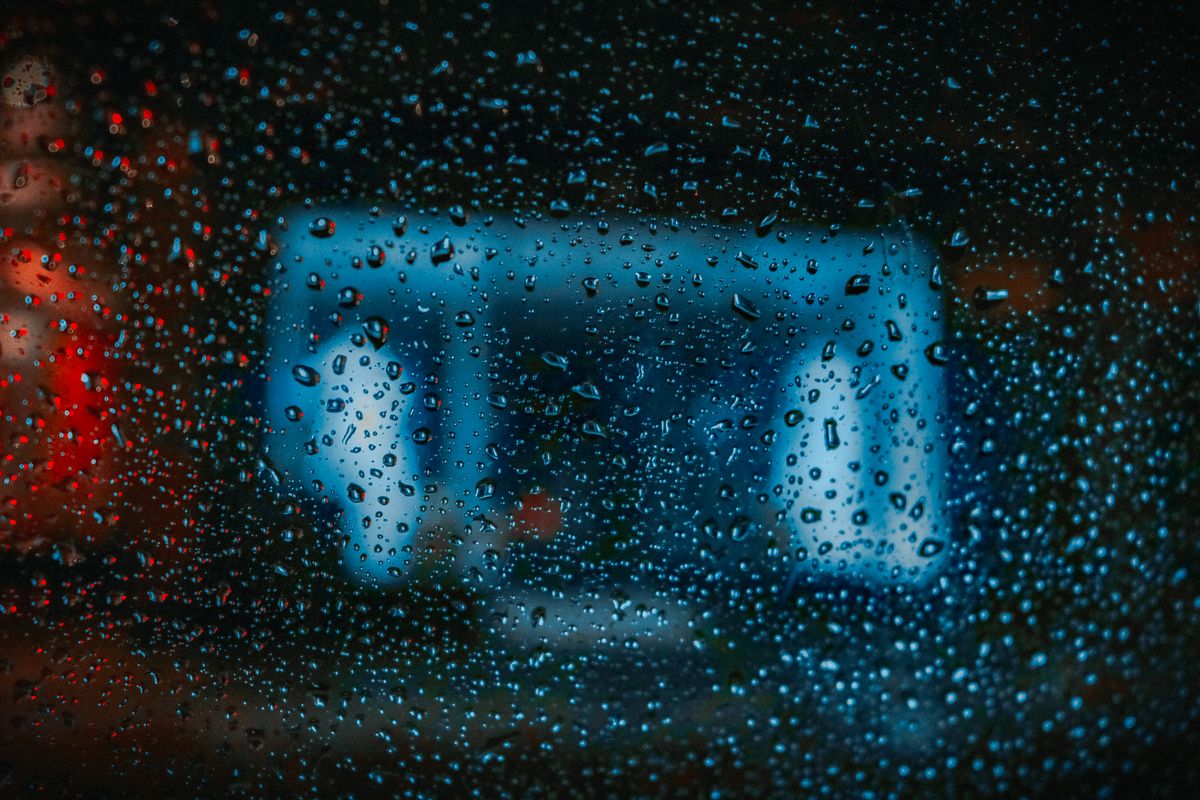 Close-up of raindrops on glass with blurred blue and red city lights in the background.