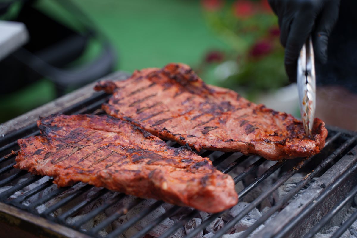 Close-up of sizzling ribs on an outdoor barbecue grill, with tongs grabbing meat.