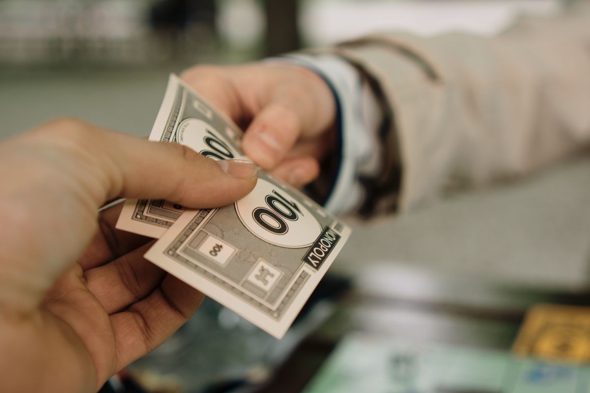 U.S. Education’s 10 Hard Truths: Reading Gaps, $800B Spending, and a System Under Pressure 2 Close-up of two hands exchanging Monopoly money, symbolizing a financial transaction.