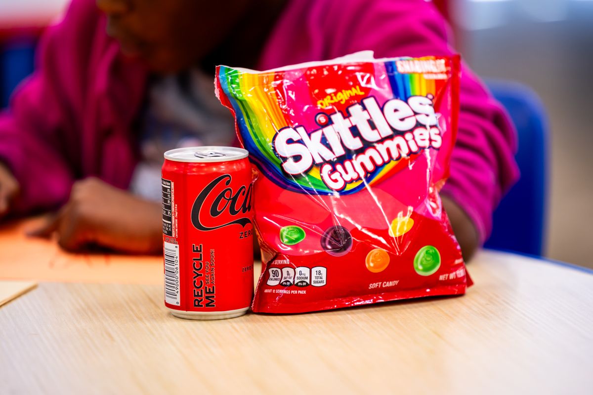 Coca-Cola Zero Sugar can and Skittles Gummies bag on a table indoors with a blurred background.