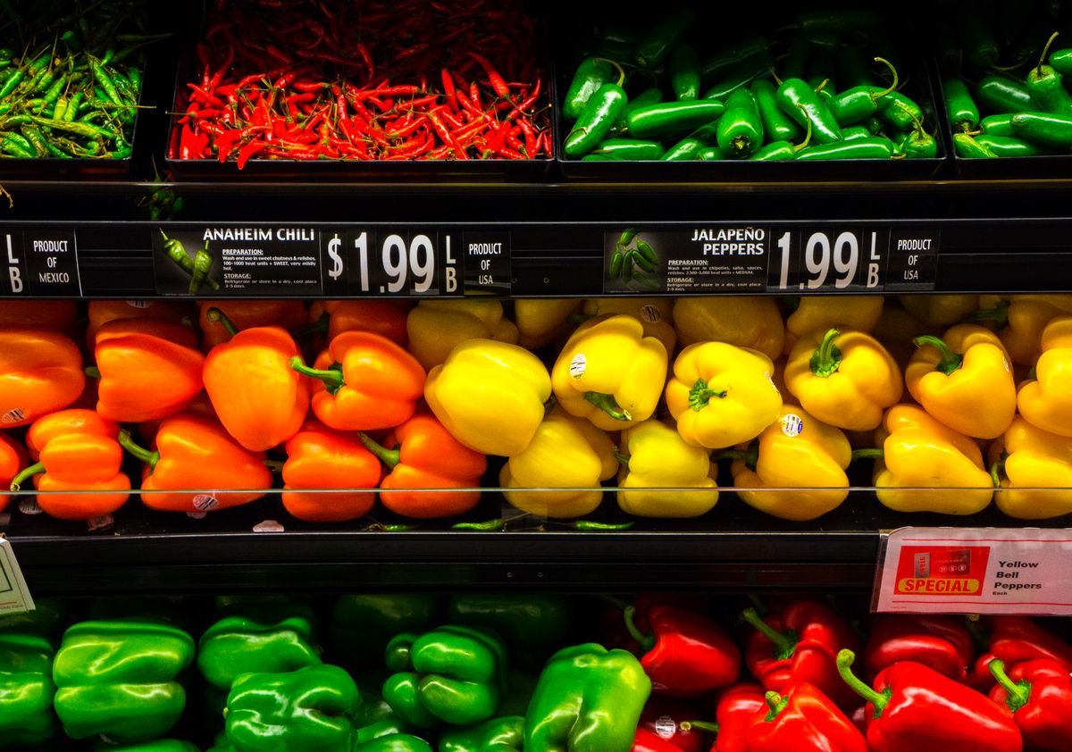 Colorful assortment of bell, jalapeño, and Anaheim peppers in a grocery store aisle.