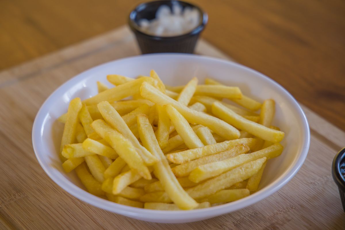 Crispy golden french fries served in a white ceramic bowl on a wooden table.