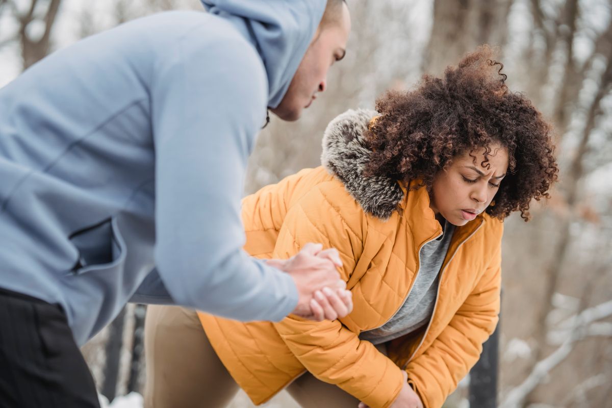 Crop instructor with hands clasped helping African American female stretching in park in winter