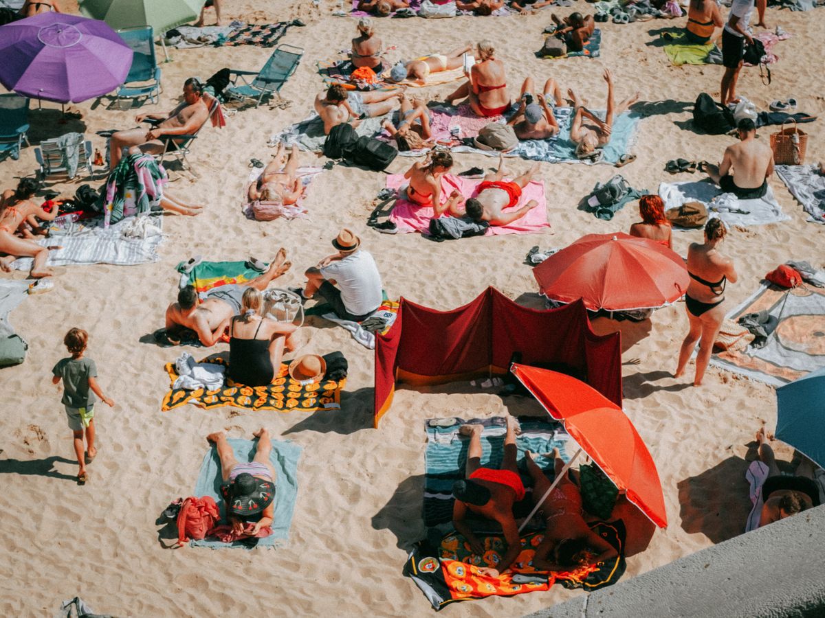 Crowded beach scene on a sunny day in Cascais, Portugal, capturing people sunbathing and enjoying leisure time.