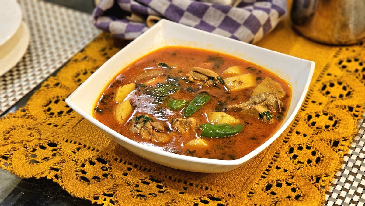 Delicious chicken and potato soup garnished with herbs in a bowl, set on a decorative tablecloth.