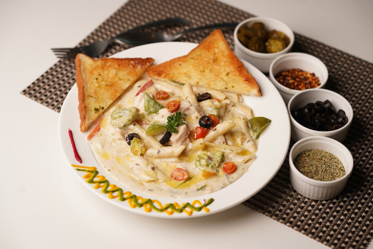 Delicious creamy pasta with toast served with olives, herbs, and peppers on a decorated plate.