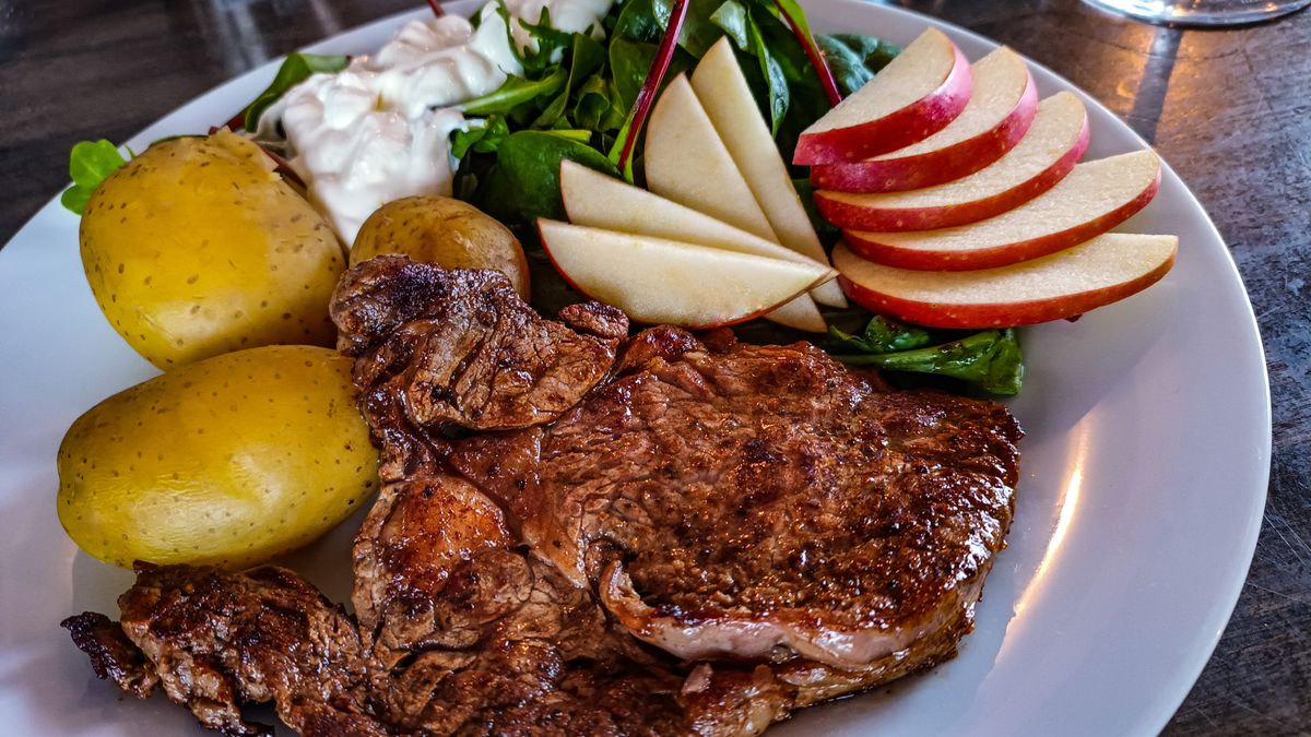 Delicious grilled steak with potatoes, fresh salad, and apple slices on a white plate.
