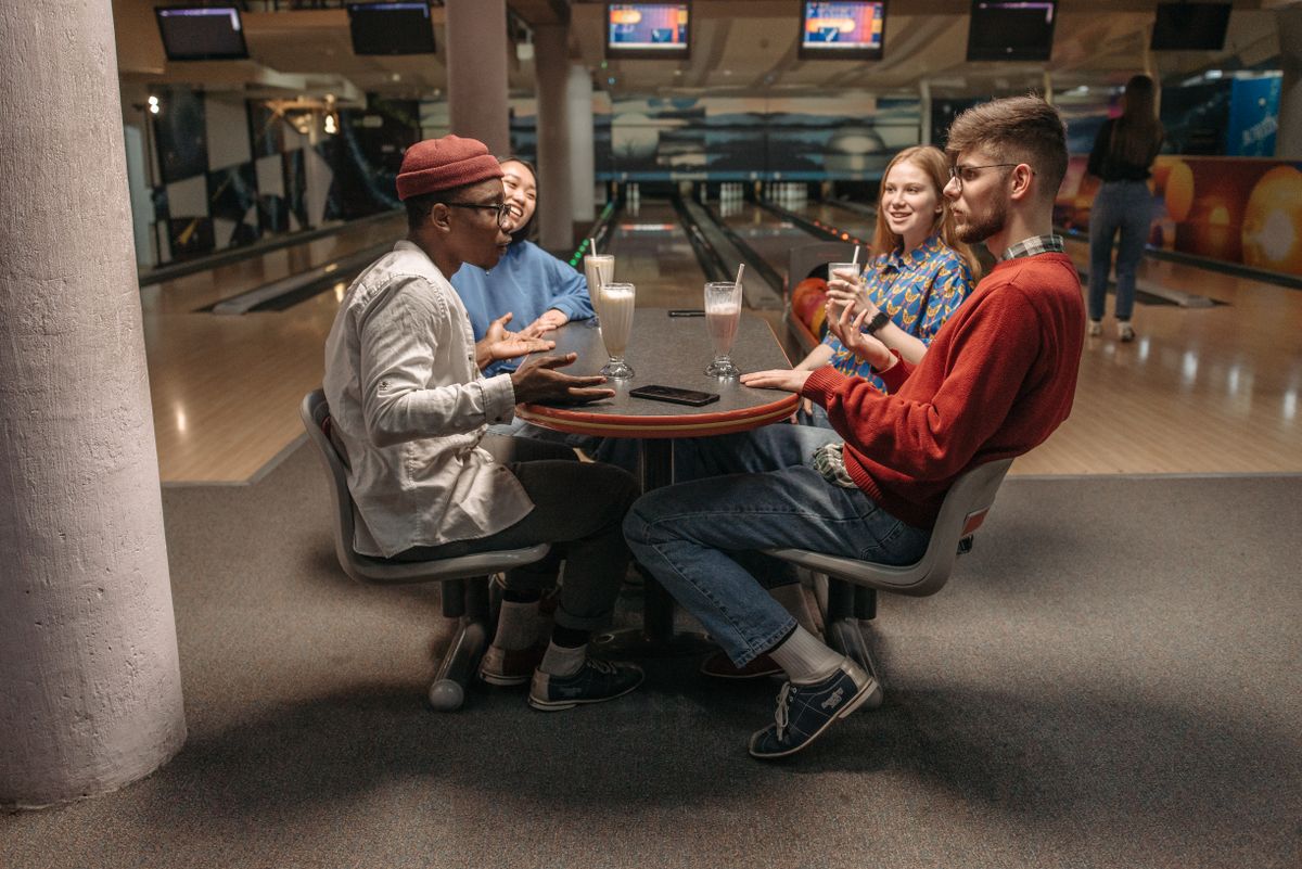 Diverse group of friends enjoying milkshakes and conversation at a bowling alley.