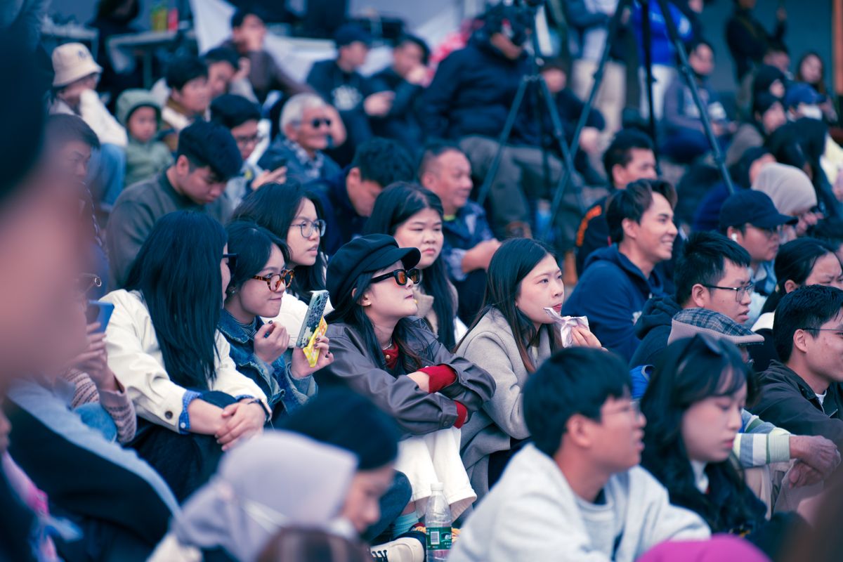 Diverse group of people enjoying a public outdoor event, focused and attentive.