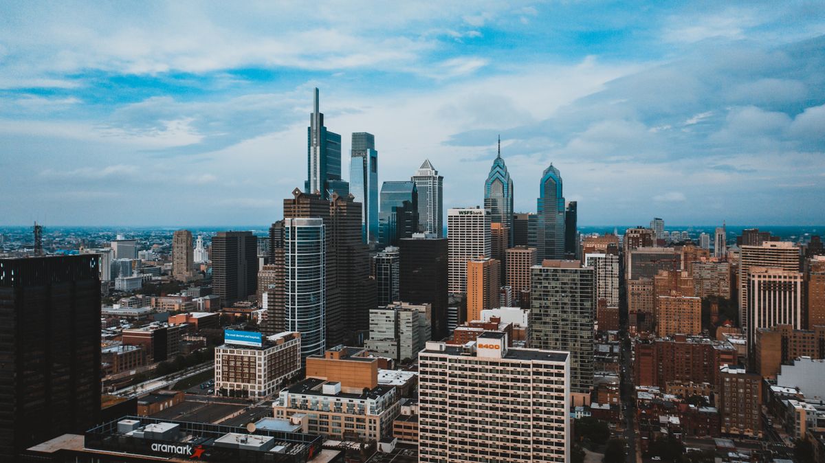 Drone view of city combining residential buildings and high steel office buildings under cloudy sky in America