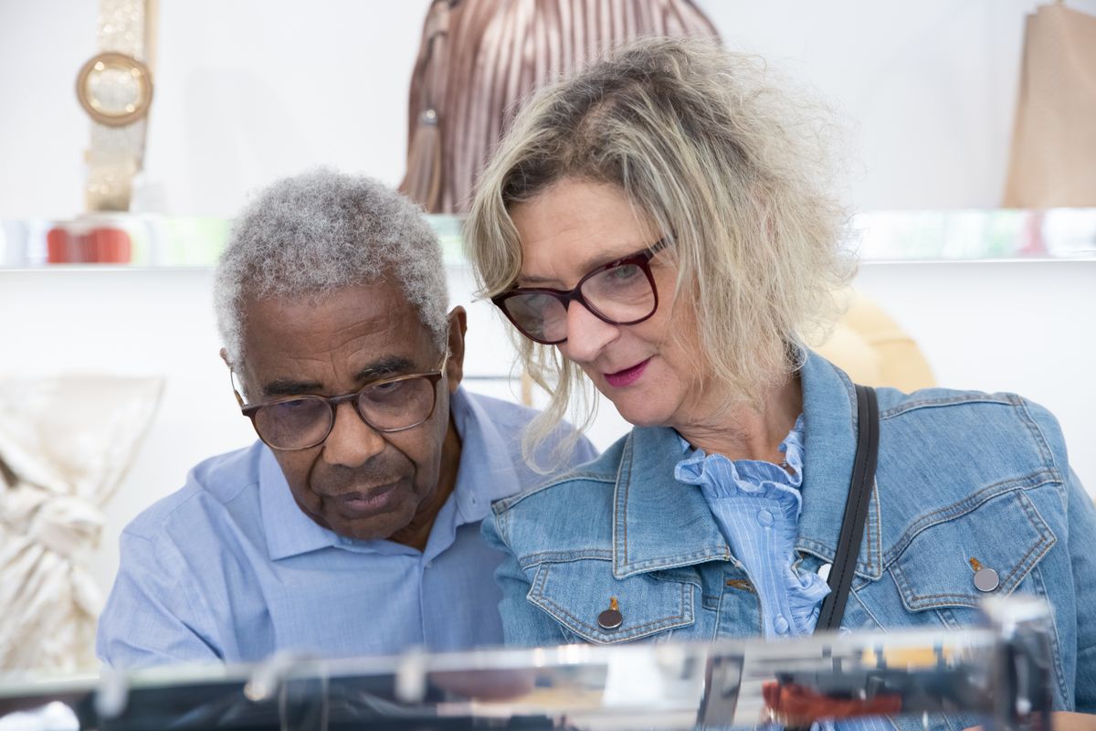 Elderly couple shopping for fashion accessories in a store, reviewing items closely.