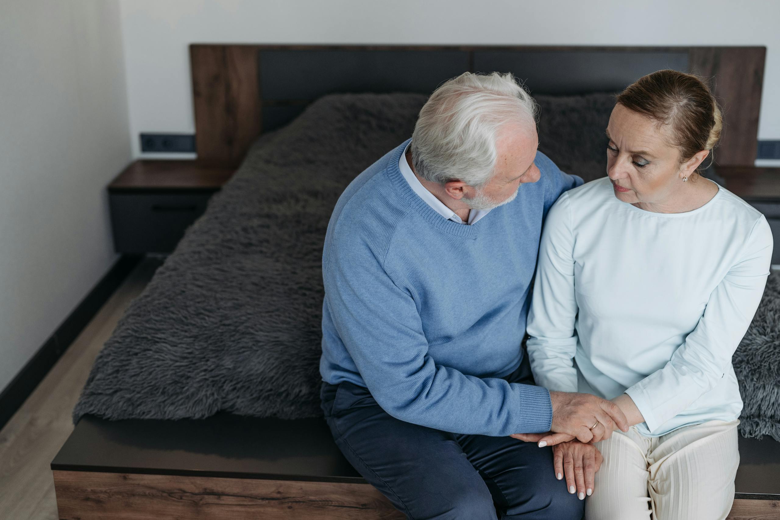 11 Harsh Truths About Marriage After 30 Years That Couples Quietly Learn 2 Elderly couple sitting on a bed, holding hands in a moment of comfort and support.
