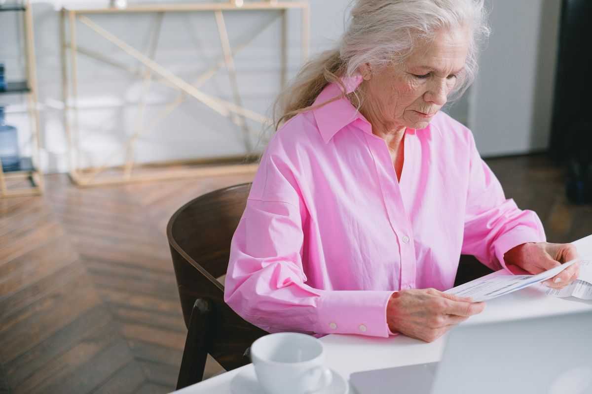 12 Everyday Habits That Will Fade With the Baby Boomer Generation 2 Elderly woman in pink shirt reading papers at home office desk, focused on work. boomer writing a check