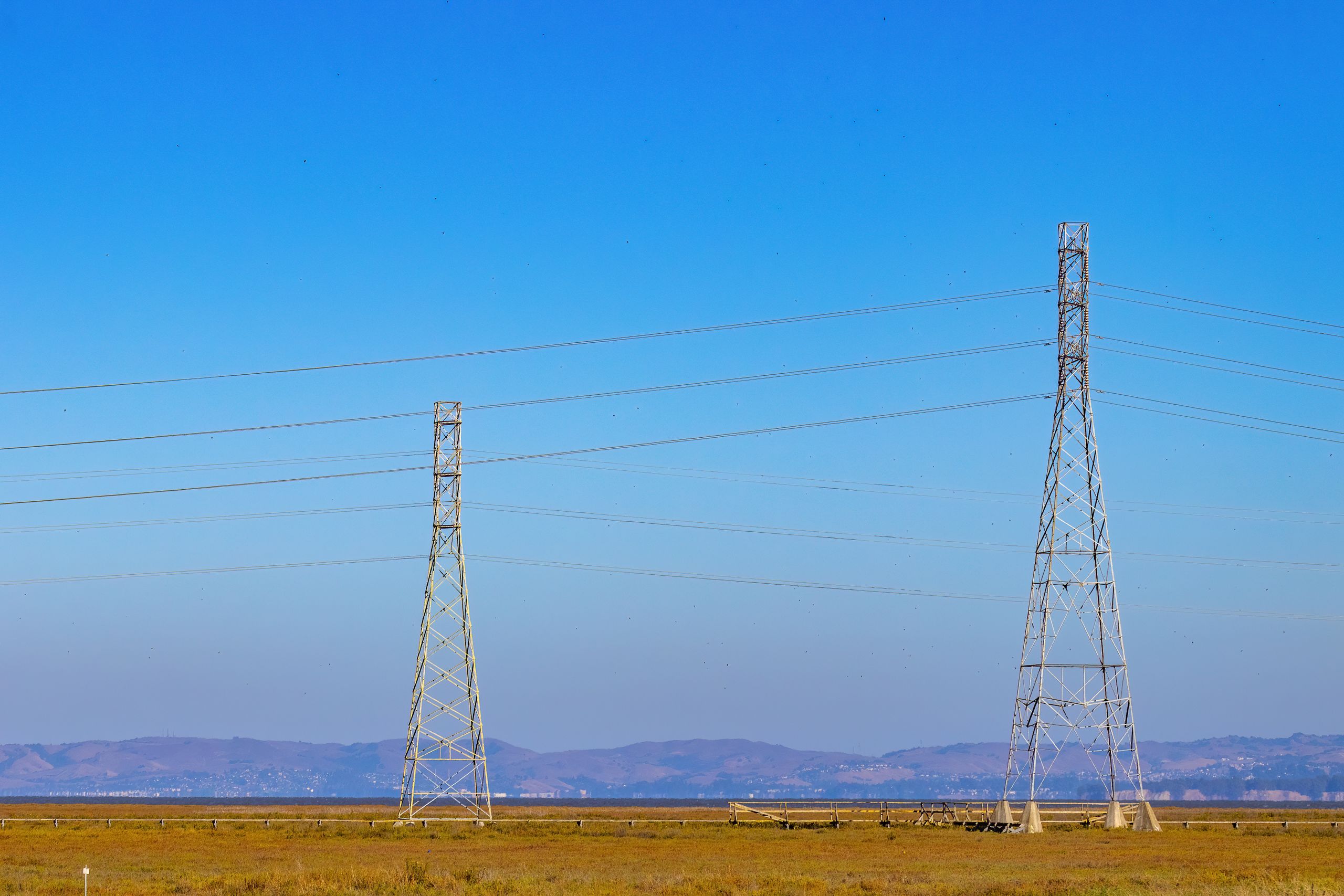 Electric towers and power lines under a clear blue sky in a natural landscape.