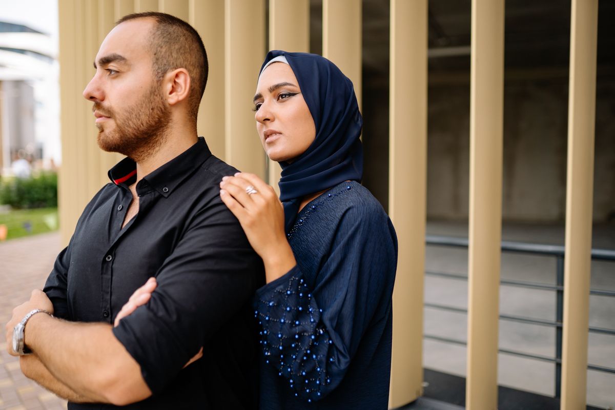 Elegant couple in urban setting, woman in hijab and man in black shirt, conveying love and partnership.