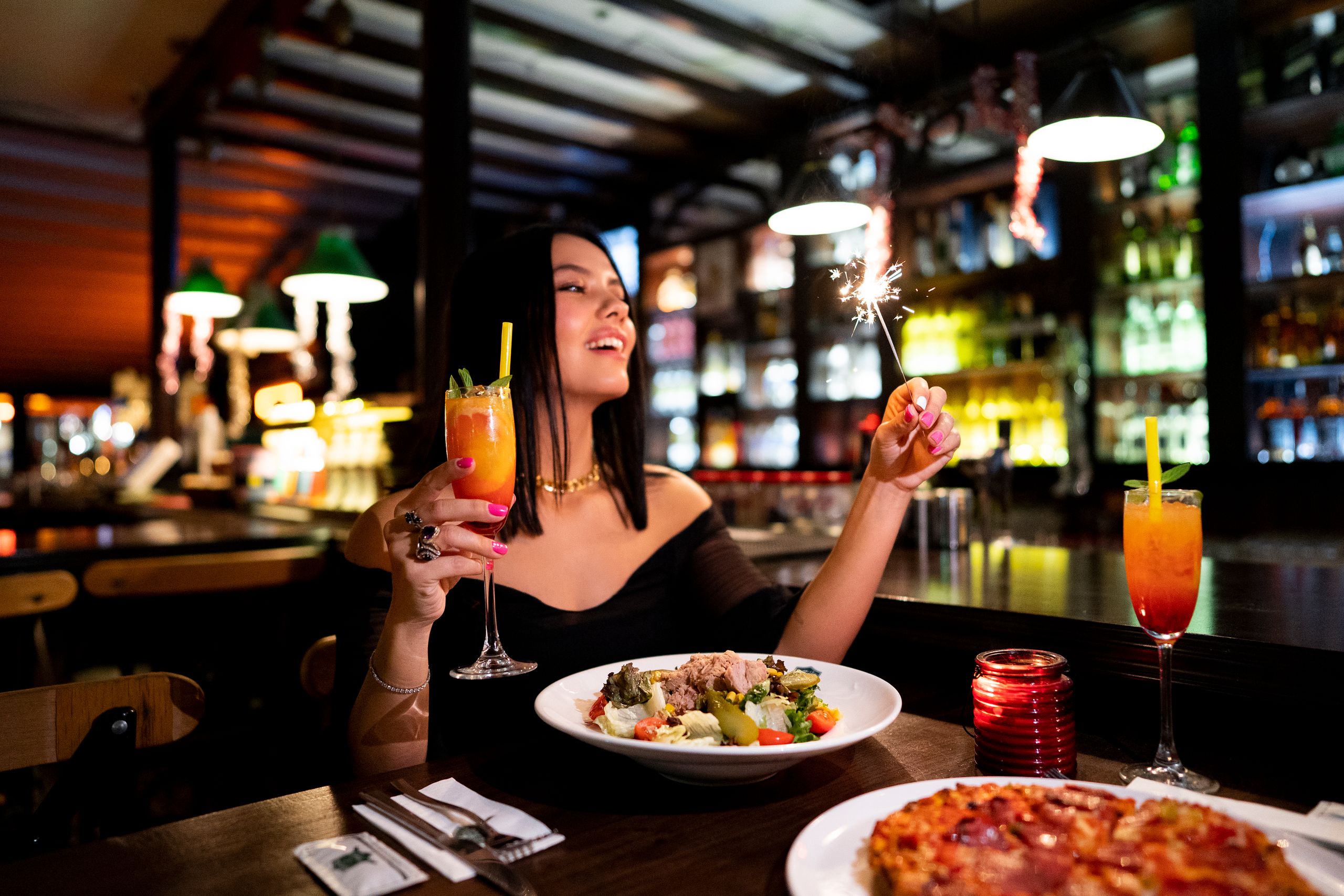 Elegant woman enjoying dinner with cocktails at an Istanbul restaurant, holding sparklers.