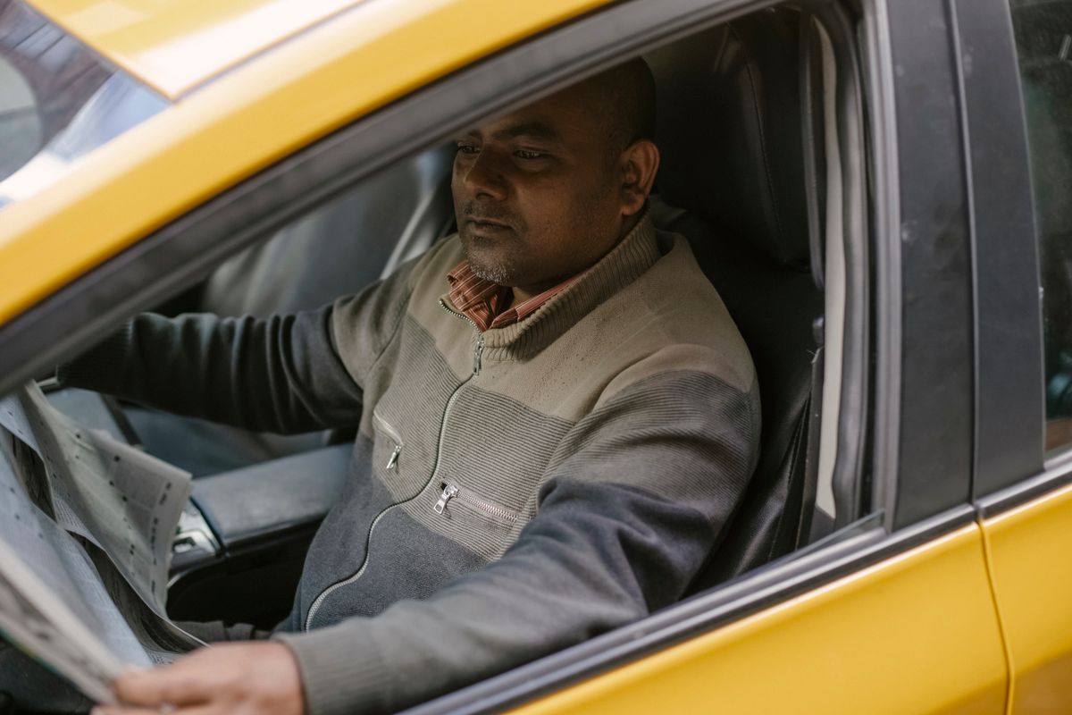 Gas Prices Are Climbing Again as Iran War Sends a Shock Through American Wallets 1 Ethnic male driver reading daily newspaper with interest while sitting in car and having break