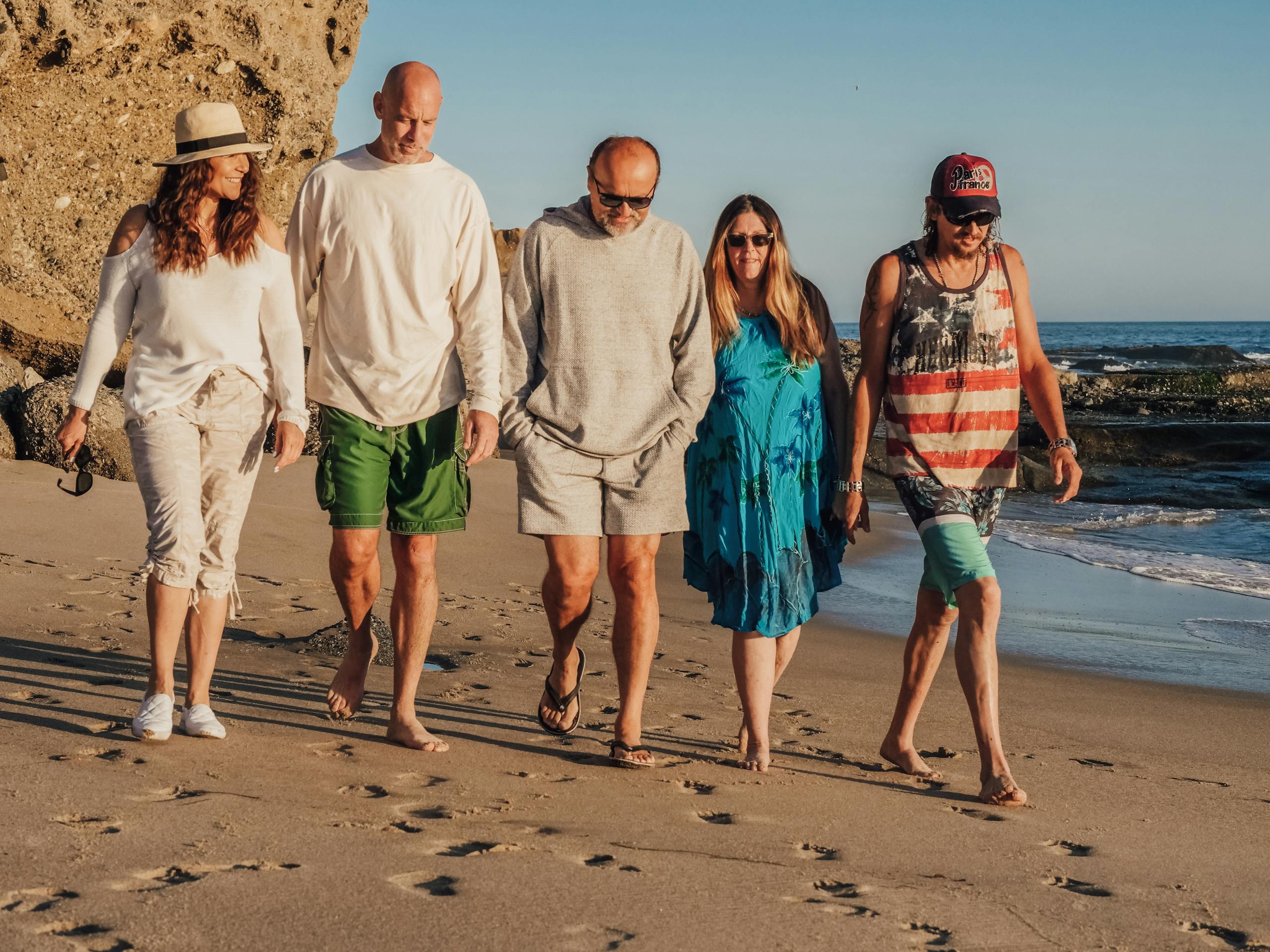 9 boomer travel habits that can drain the fun out of any trip 3 Five friends walk along a sunny beach, enjoying a joyful summer day together.