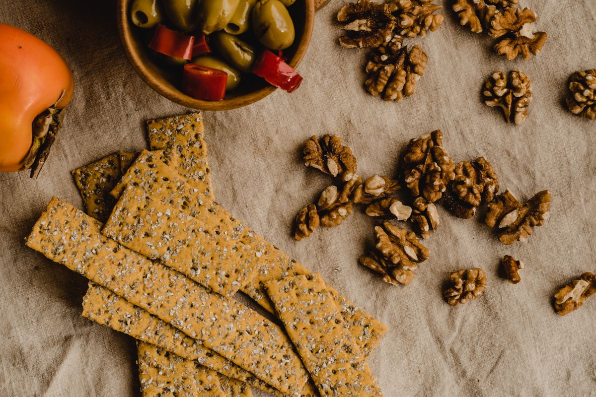 Flat lay of crackers, walnuts, and olives on a cloth, perfect for a rustic snack board theme.