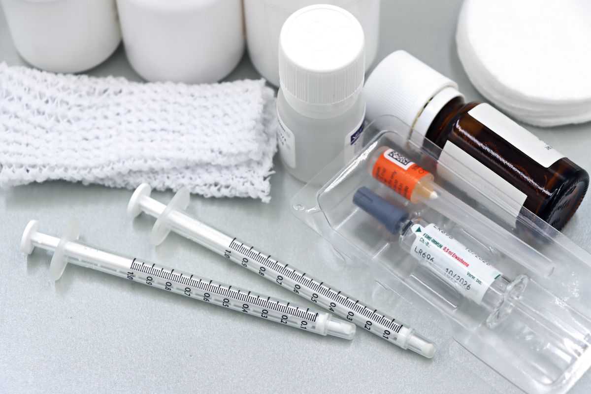 Flat lay of medical tools and vaccines, including syringes and bottles, on a white surface.