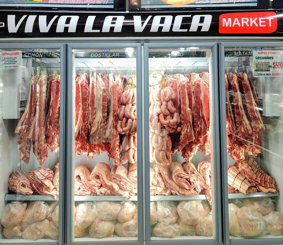 Fresh cuts of meat and sausages in a well-lit market refrigerator display.