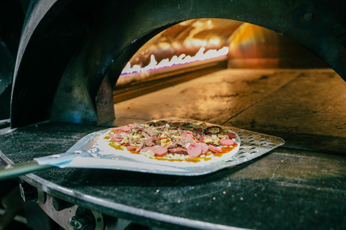 Fresh pizza being prepared in a traditional wood-fired stone oven, capturing authentic Italian cooking.