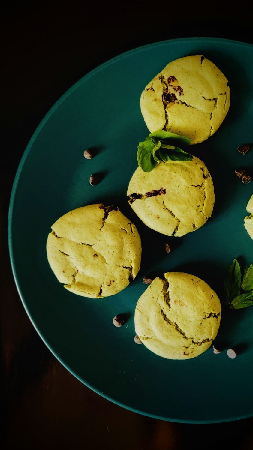 Freshly baked mint chocolate chip cookies arranged on teal plate.