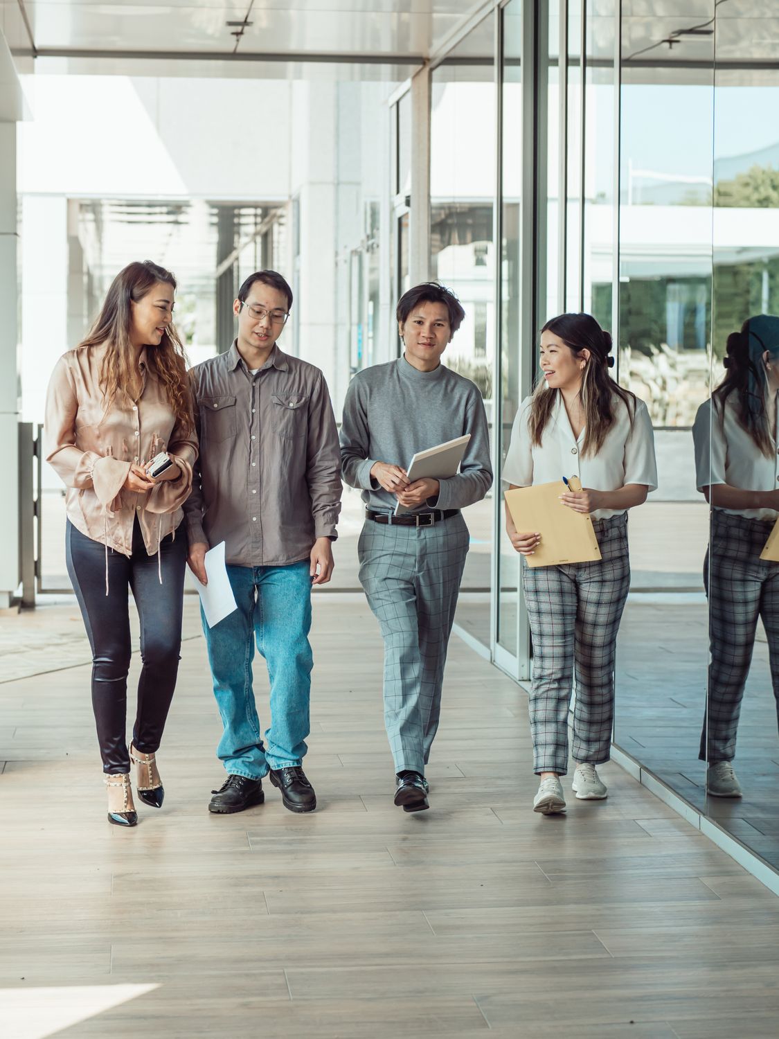The Commute Is Back, But Workers Are Not Going Back to the Old Office Life 2 Group of four diverse colleagues walking outdoors, discussing work and holding documents.