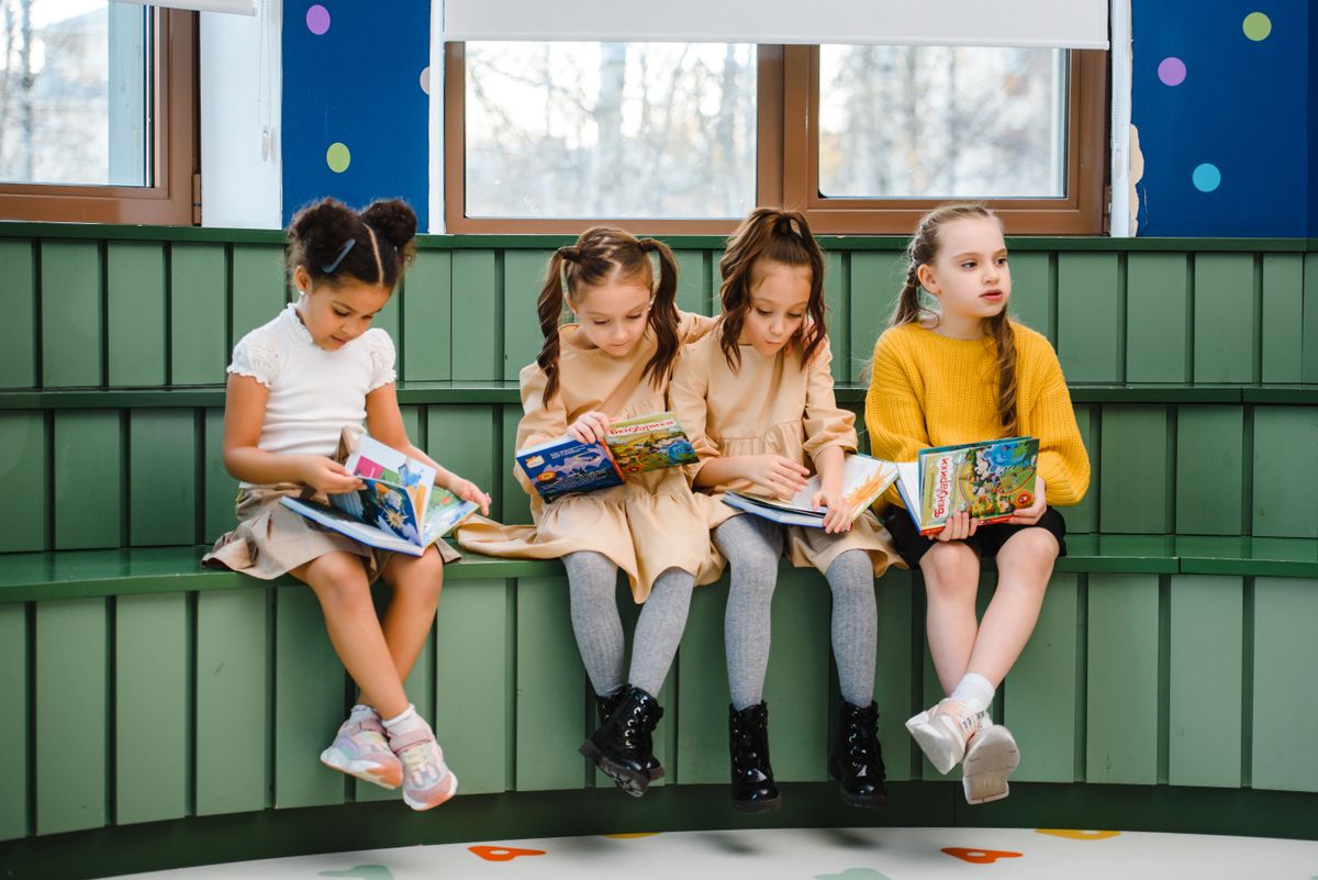 Group of young girls sitting indoors, reading and studying in a classroom setting.