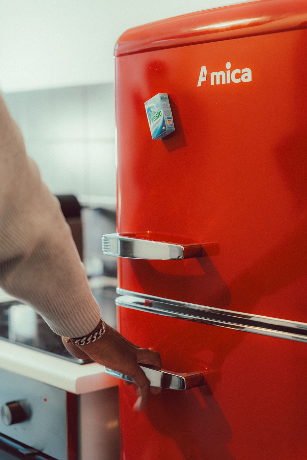 Hand opening a vibrant red vintage refrigerator in a modern kitchen setting.