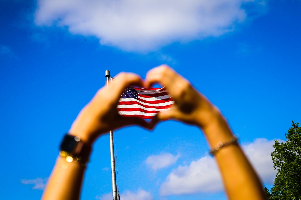 Most Americans Struggle to Answer These 10 Simple Questions About Their Own Country 1 Hands form a heart shape around an American flag against a vibrant blue sky, symbolizing patriotism and freedom.