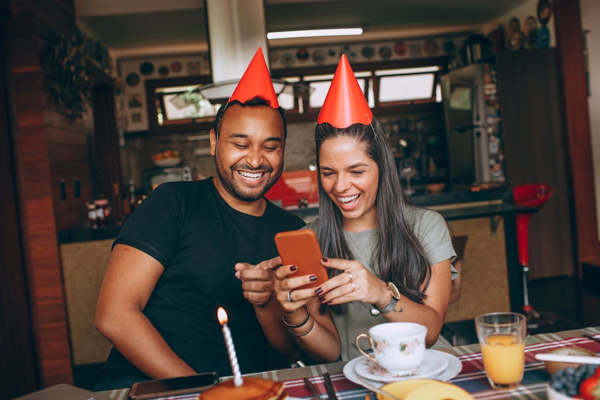 Happy couple with party hats celebrating a birthday at home, enjoying a cheerful moment.
