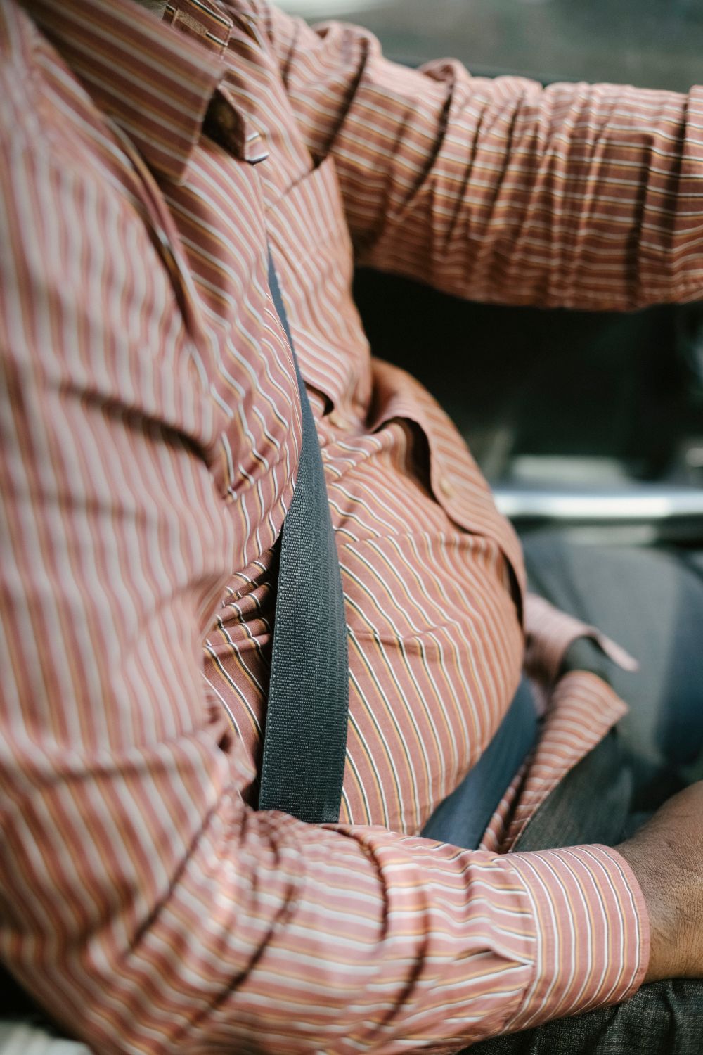 High angle side view of crop anonymous ethnic man in casual wear with fastened seat belt driving vehicle