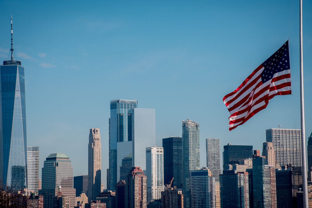 Iconic New York City skyline with American flag flying under clear blue sky.