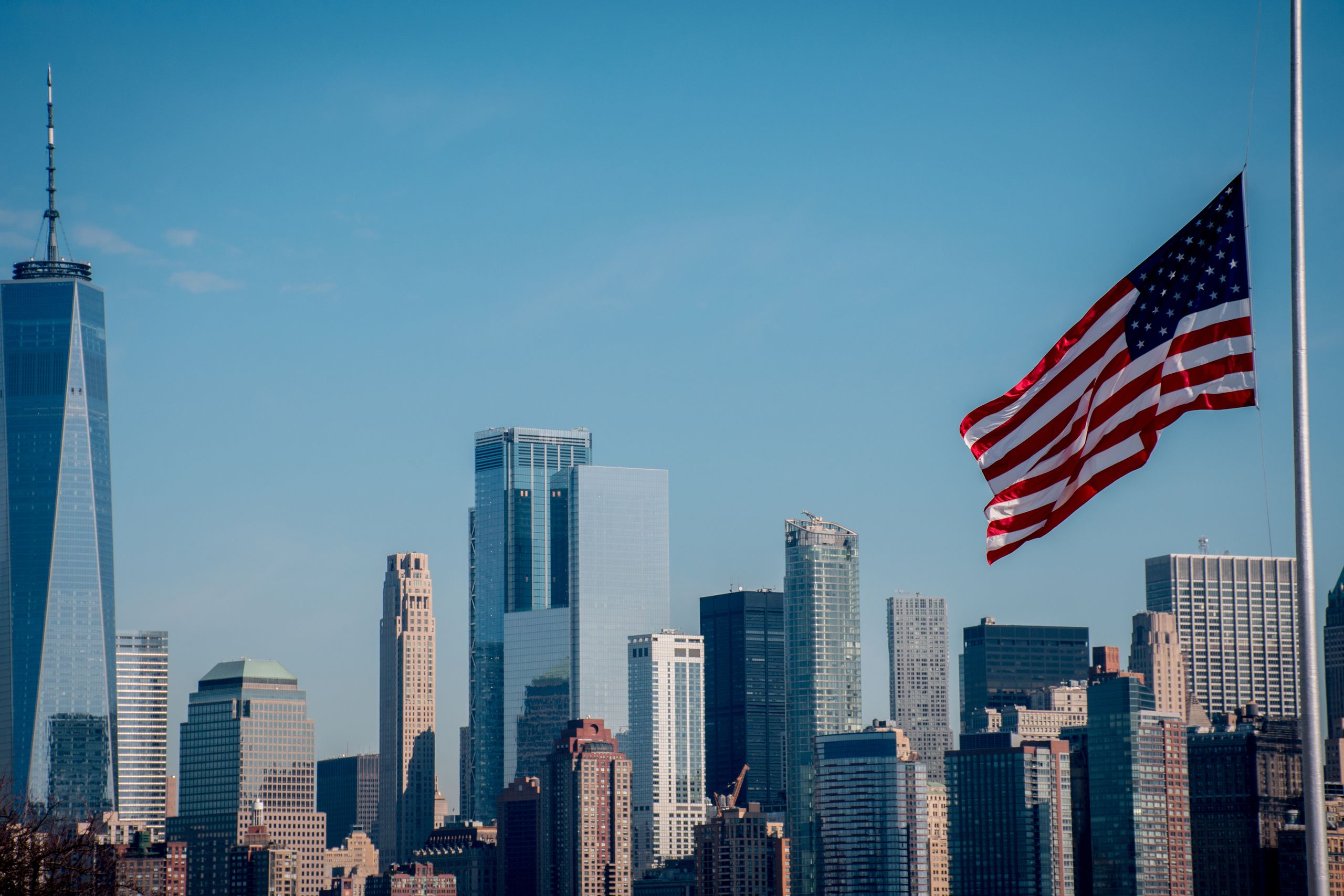 Iconic New York City skyline with American flag flying under clear blue sky.