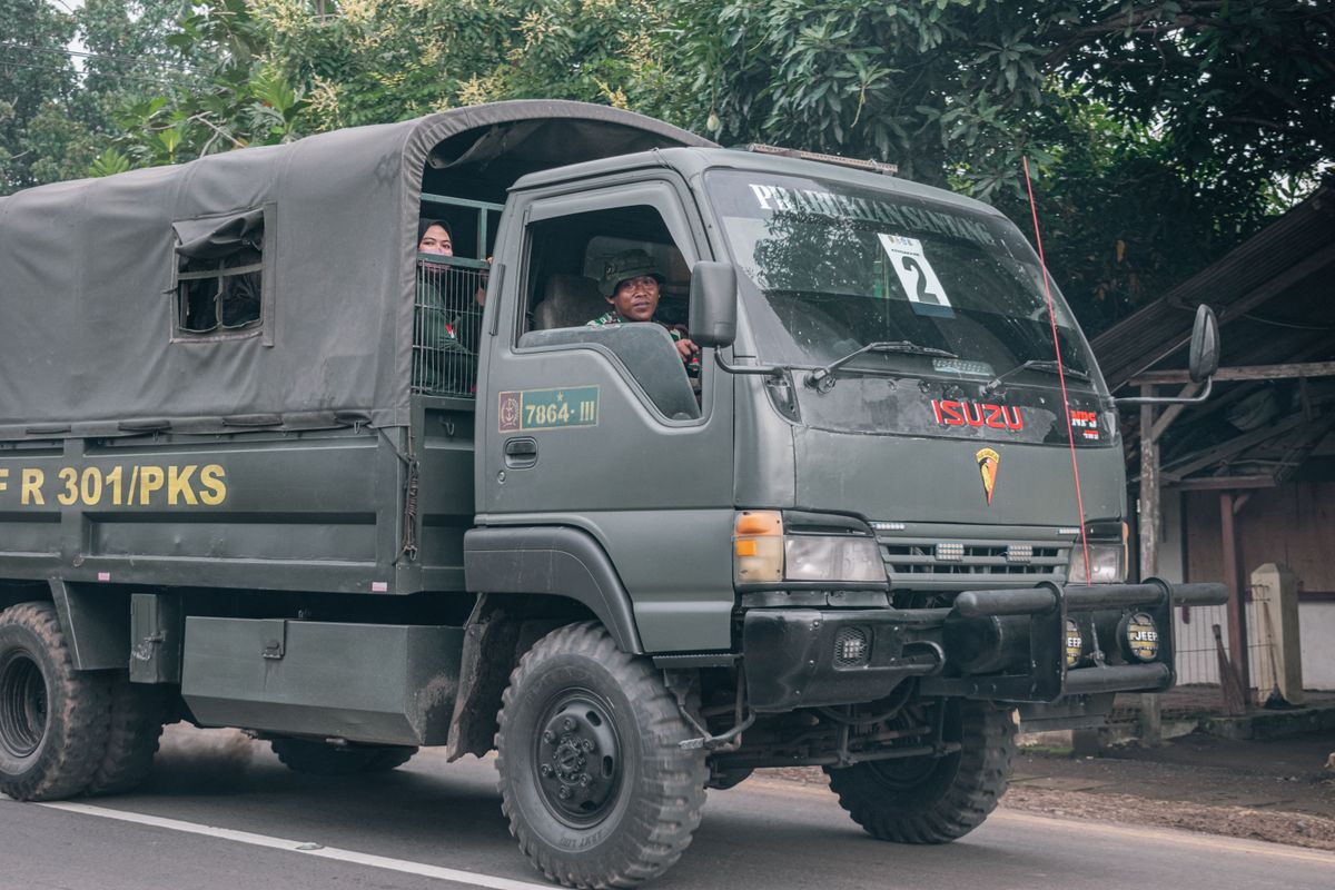 Isuzu military truck with soldiers drives on a rural road, showcasing army presence.