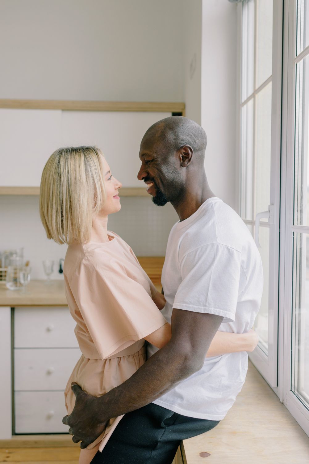 Joyful interracial couple embracing while sitting in a bright modern kitchen, smiling and enjoying the moment.