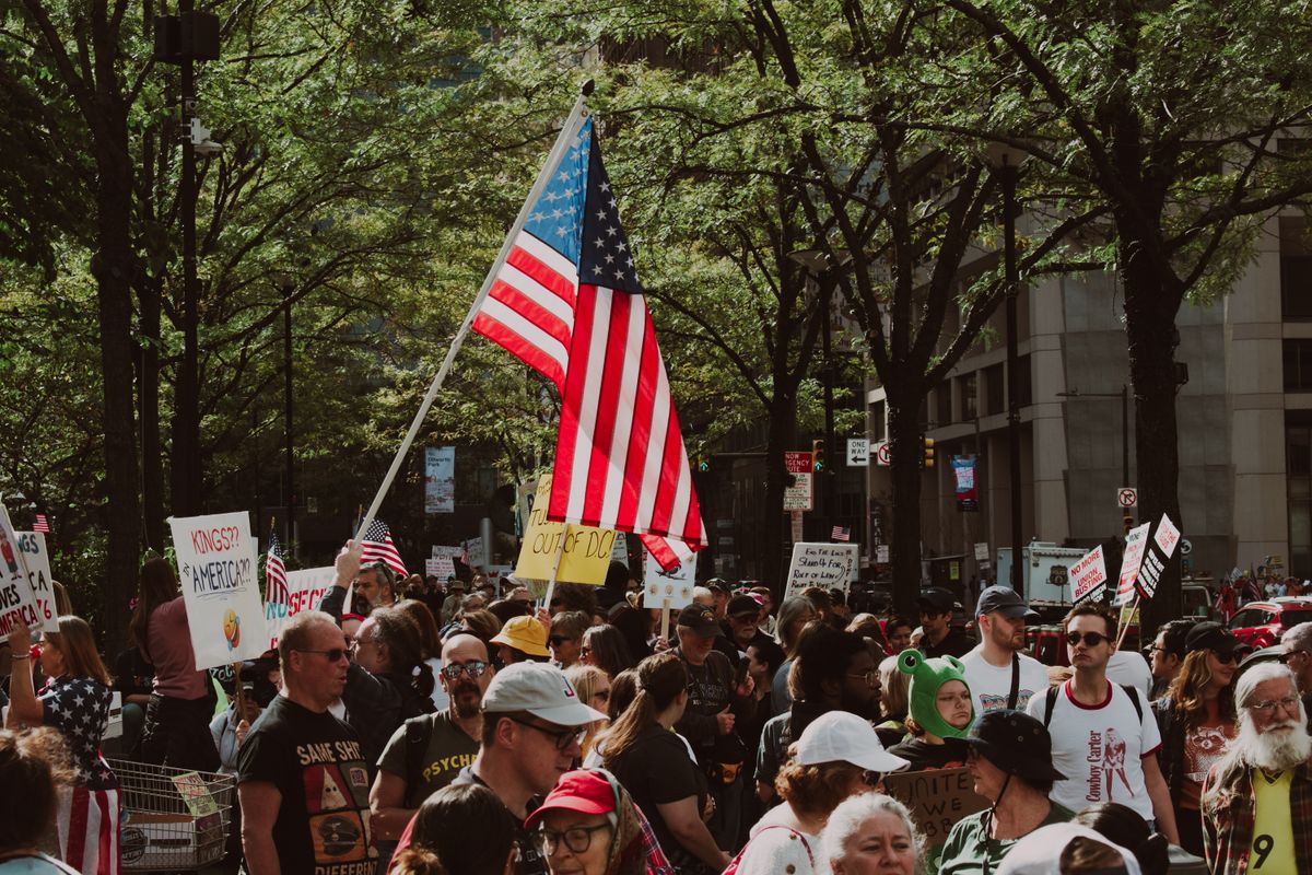 New Poll Shows American Pride Falling as U.S. Democracy, History and Identity Face a 250th Anniversary Test 2 Large diverse crowd gathered outdoors for a protest holding signs and an American flag.