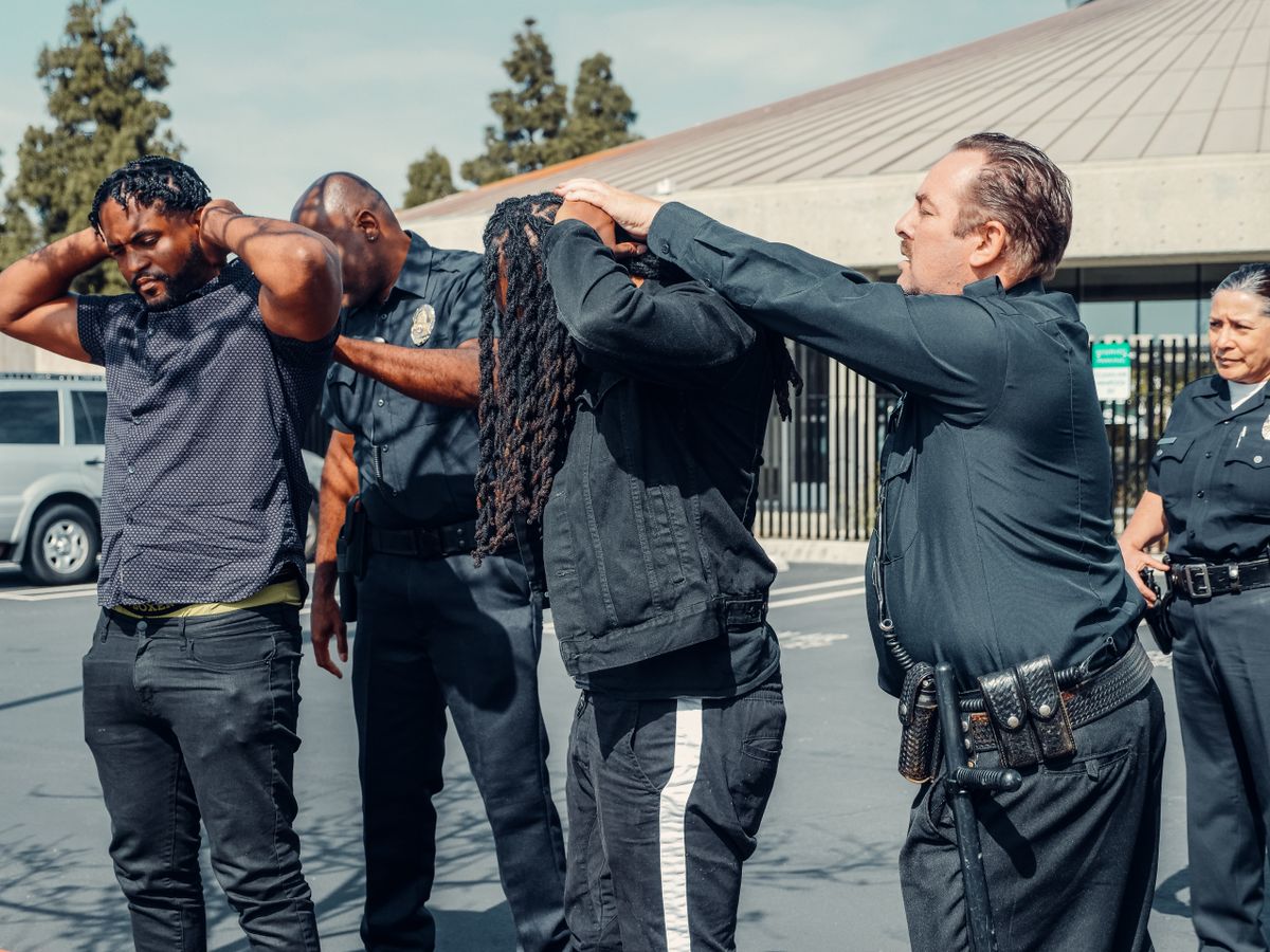 Law enforcement officers performing a pat-down on two individuals in an urban setting.