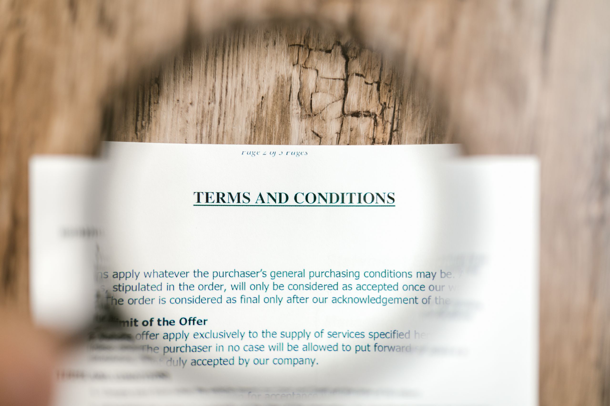 Older Americans Paid Into the System. Now Their Benefits Feel Hidden in Fine Print 1 Magnifying glass focusing on terms and conditions document on wooden surface.
