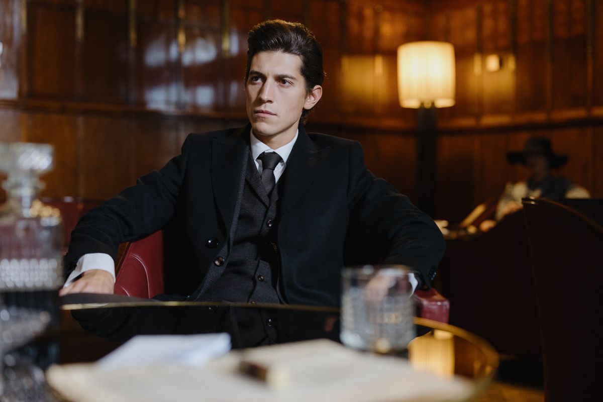 Man in a black formal suit sitting in a vintage room, exuding sophistication and elegance.