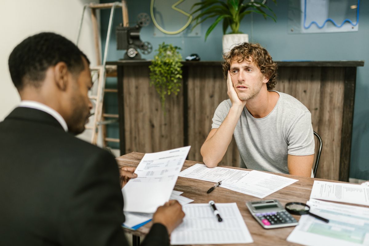 What Happens If You Do Not Pay a Deceased Person’s Credit Card Debt 3 Man in office, appearing stressed during paperwork discussion, sitting opposite professional.