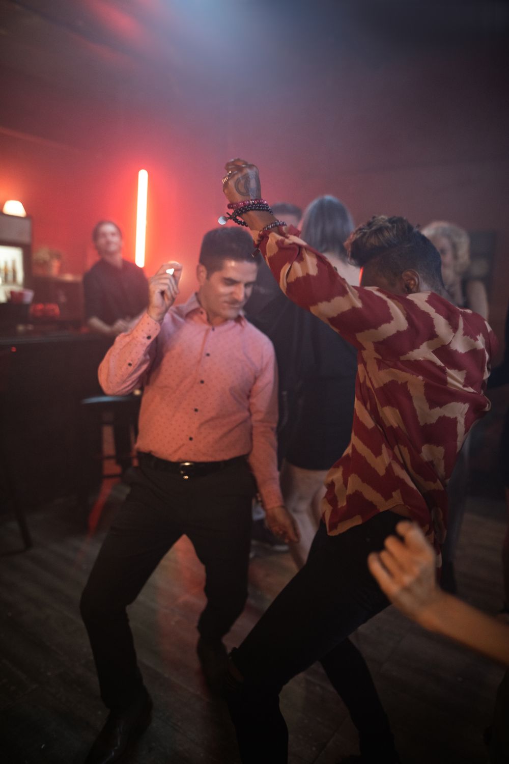 Men dancing energetically in a vibrant nightclub setting with colorful lighting.