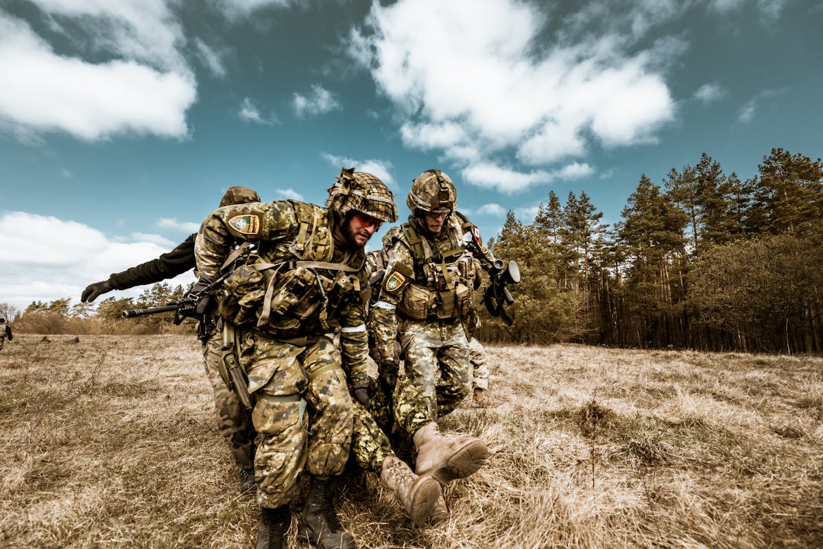 Military personnel actively engaged in outdoor rescue operation on grassy field, showcasing teamwork and bravery.